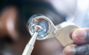 A Black jeweler holding a diamond up to a microscope with a pair of needle-nosed pliers. They're looking at diamond clarity.