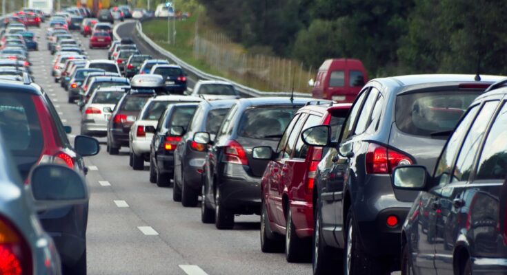 A three-lane highway completely backed up with vehicles in a traffic jam in the middle of the day.