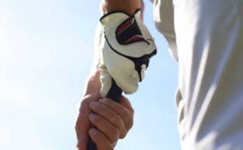 A close-up view of a pair of hands, one with a golf glove and one without, gripping the shaft of a golf club.