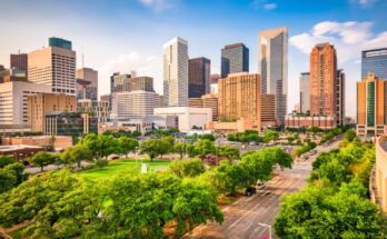 The Houston skyline in the late afternoon with the sun shining on skyscrapers and trees lining the roads.