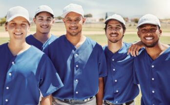 Members of an adult softball team wearing blue and gray uniforms. They're looking toward the camera and smiling.