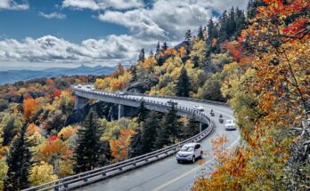 A view of the Great Smoky Mountains in the fall with cars on the winding highway. The foliage is changing colors.