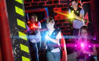 A young boy and a young girl stand in front of an adult man and woman while pointing their laser guns during laser tag.