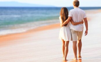 A couple strolling along a sandy beach at sunset, surrounded by gentle waves and a warm, golden glow.