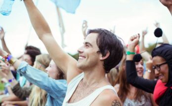 A man standing at the barricade in a crowd at a music festival, raising his arm and holding a water bottle.