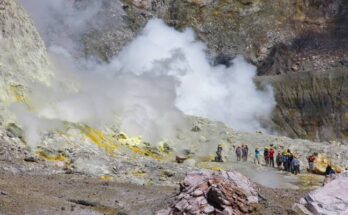 A group of people walking on the trails of a volcano as clouds of steam rise up from the crevices ahead of them.