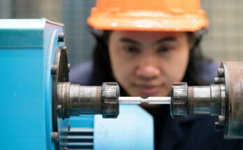 An engineer looks closely at the metal connecting piece of a machine that joins two sides with rounded pieces.