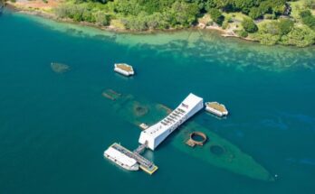 A distant aerial view of USS Arizona war memorial in Hawaii. The submerged ship is visible beneath the water’s surface.