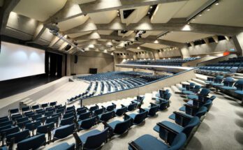 The interior of an event space with a large screen at the bottom and rows of chairs lining the auditorium.