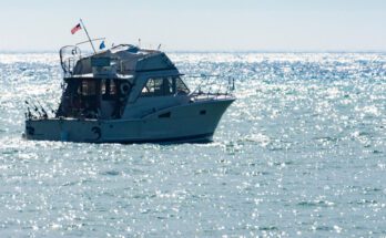 A fishing charter boat with the engines off in the middle of a large body of water with the sun beating down overhead.