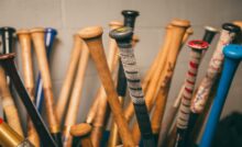 The handles of dozens of baseball bats grouped upright. Some are colorful and some have grip tape.