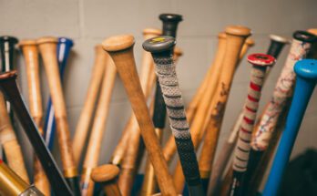 The handles of dozens of baseball bats grouped upright. Some are colorful and some have grip tape.