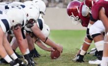 A scrimmage line before a play in a North American football game. The blurred stands beyond the men are packed.