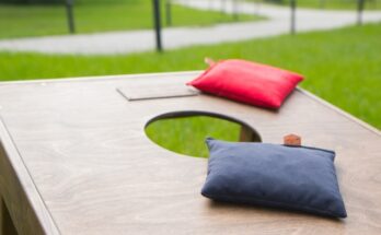 A close-up view shows a red and a blue bean bag lying on the flat surface of a wooden cornhole board.