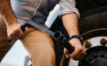 A headless shot of a man in a dress shirt using a socket wrench to tighten the bolts on a semi-truck’s tire.