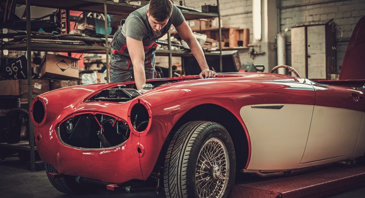A car mechanic hovering over the top of the front engine with his hand down in the compartment. The car is red.