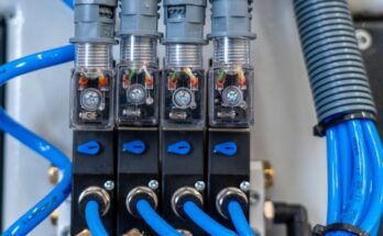 A close-up view shows four black solenoid valves with blue tubes attached, lined up next to each other.