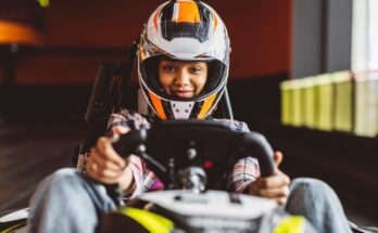 A close-up view shows a person wearing a white helmet while sitting in a go-kart on an indoor track.