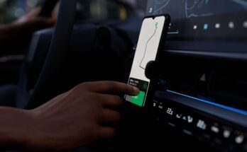 A dark vehicle with a phone attached to a holder. The screen shows a map, and someone taps their finger on it.