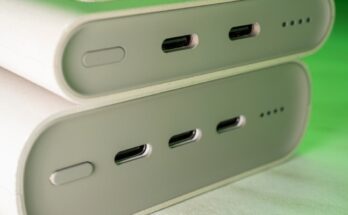 Two portable power banks are stacked on each other and are illuminated by a green light. The power banks have three ports.