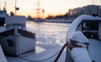 A close-up and focus on the mooring bollard on the boat that's covered by snow during a winter sunset.
