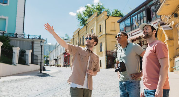 A group of three men on a vacation together. Two are receiving a tour from the other man as he points to a location.