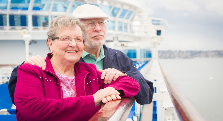 A woman wearing a pink sweater standing next to a man wearing a white hat leaning against the handrail of a cruise ship.